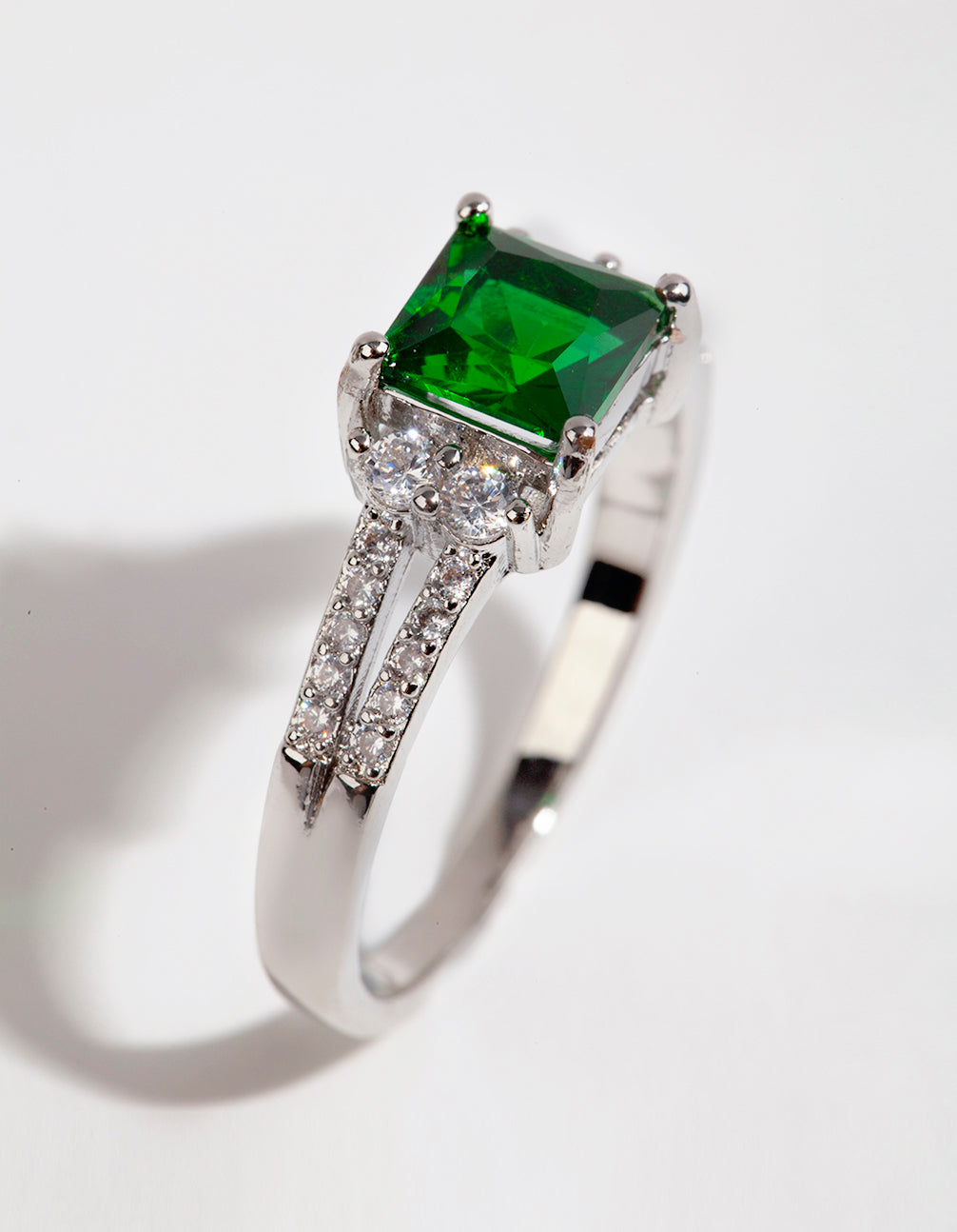 Highlighting a silver square emerald cubic zirconia ring with green stone and prong setting side detail view