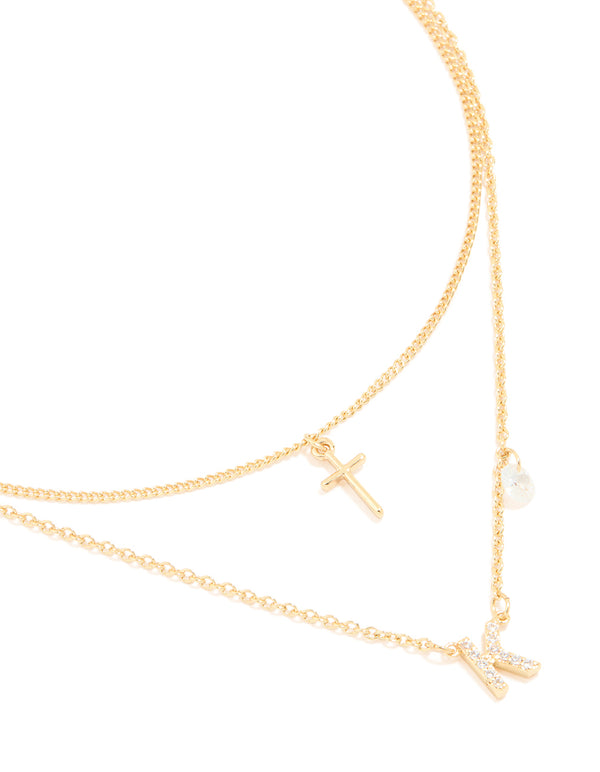 Showcasing a layered necklace with cross and letter K charms crafted from gold plated material featuring cubic zirconia in a statement style close up view