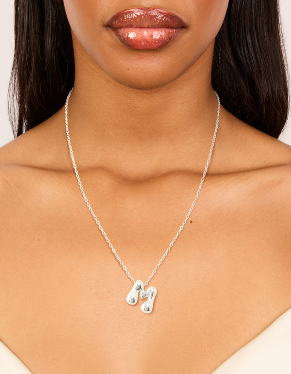 Crafted from waterproof stainless steel, this dainty initial pendant necklace in silver features a large bubble letter M on neck view
