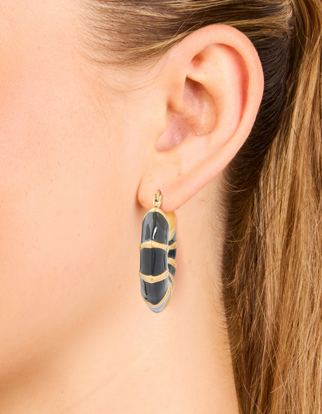 Designed with waterproof stainless steel, these statement hoop earrings feature black enamel bamboo detailing and plated finish in gold on ear view
