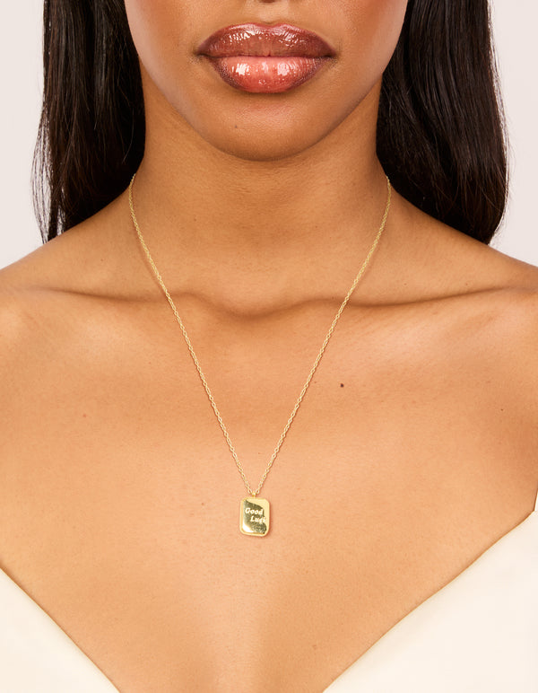 Showcasing a waterproof good luck pendant necklace crafted from gold plated stainless steel with script detailing in a dainty style on neck view