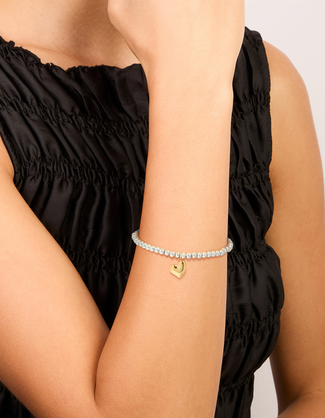 Showcasing a waterproof stainless steel heart pendant stretch bracelet with beads gold plated accents in silver on wrist view