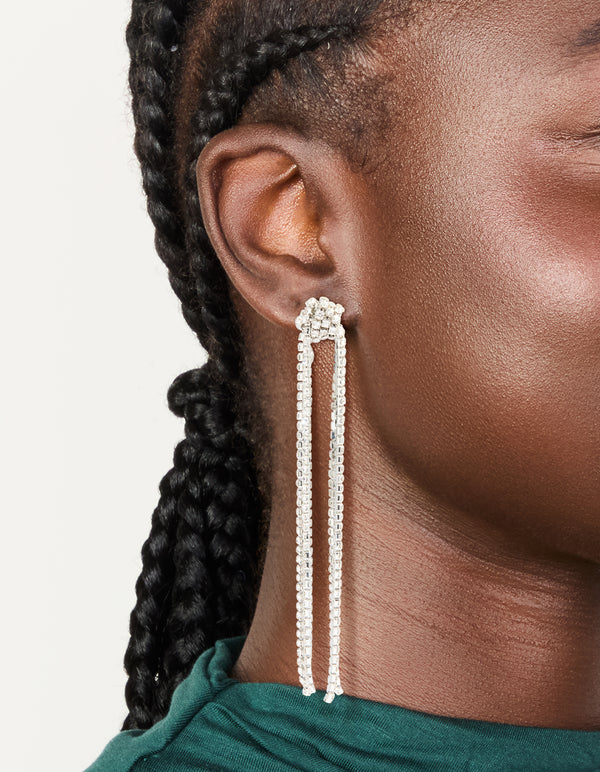 Showcasing statement diamante knotted tassel drop earrings in silver on ear view