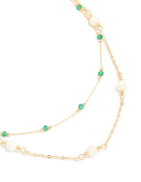 This gold plated layered necklace features beads with emerald stone and pearl accents close up view