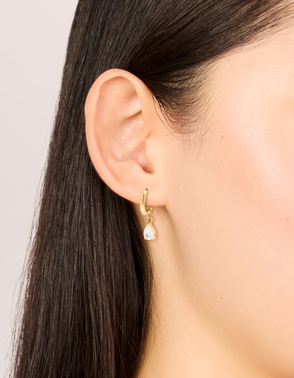 Showcasing waterproof dainty huggie earrings with pear cut cubic zirconia charm in gold plated stainless steel on ear view