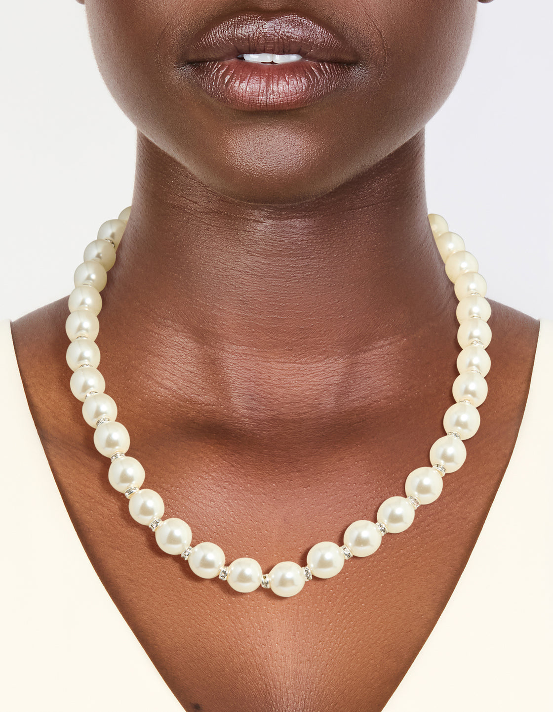 Showcasing a silver plated diamante and pearl necklace worn around the neck with ivory beads on neck view