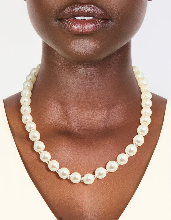 Showcasing a silver plated diamante and pearl necklace worn around the neck with ivory beads on neck view