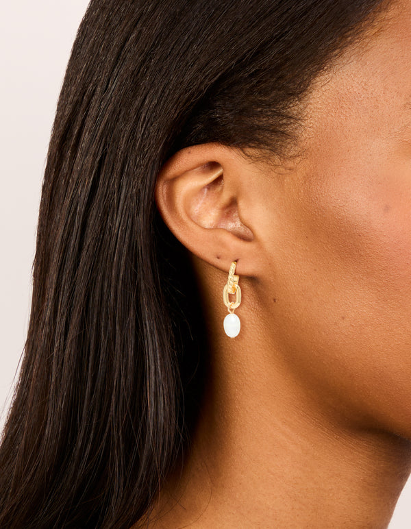 Showcasing gold plated textured freshwater pearl drop huggie earrings on ear view