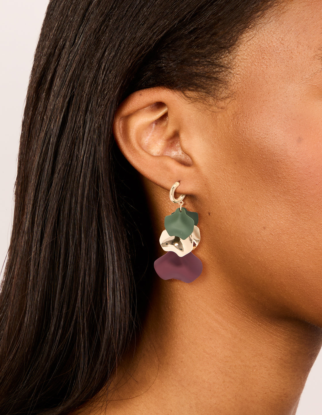 Showcasing statement drop earrings with floral five petal design and charm feature in green and purple on ear view