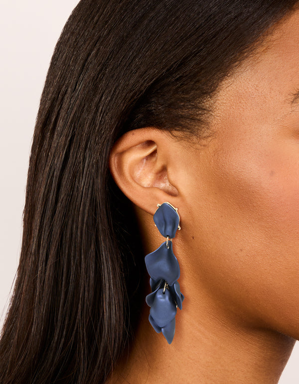 Showcasing navy blue coated metal flower petal drop earrings with gold accents with on ear view