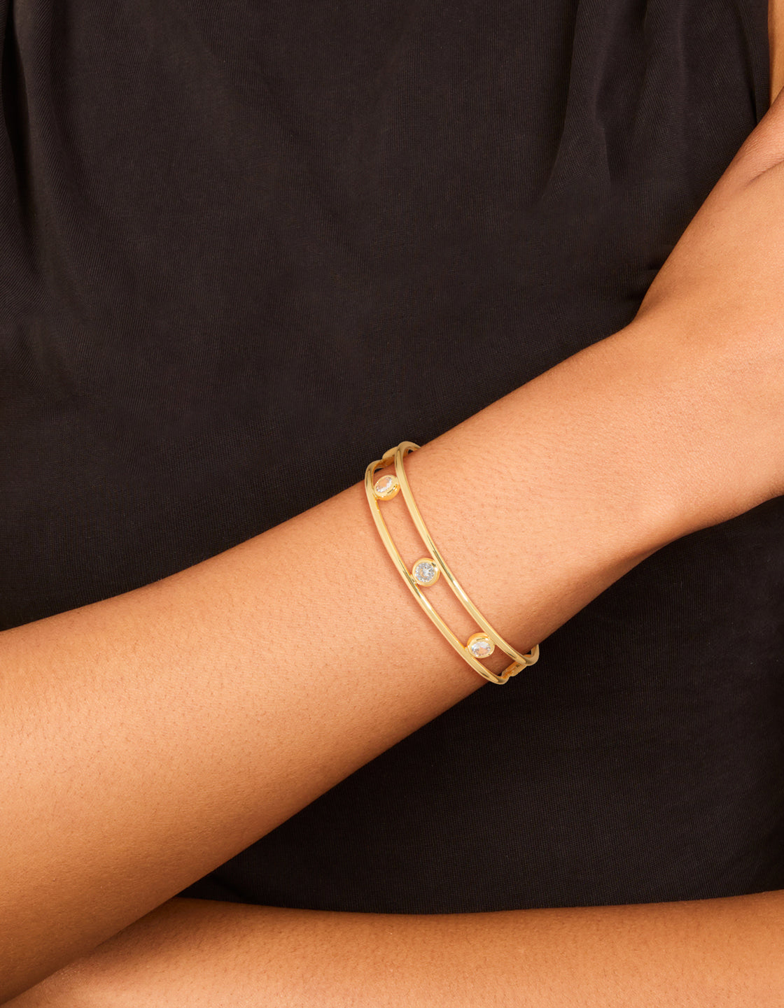 Featuring cubic zirconia stones in bezel settings, this gold plated brass statement bangle cuff is shown on wrist view