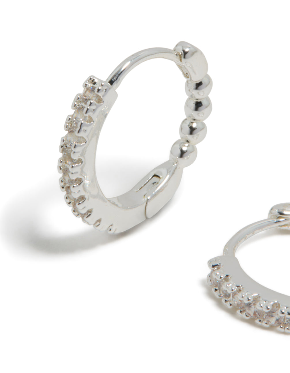 Featuring skinny huggie earrings in silver plated finish with cubic zirconia hoop closure close up view