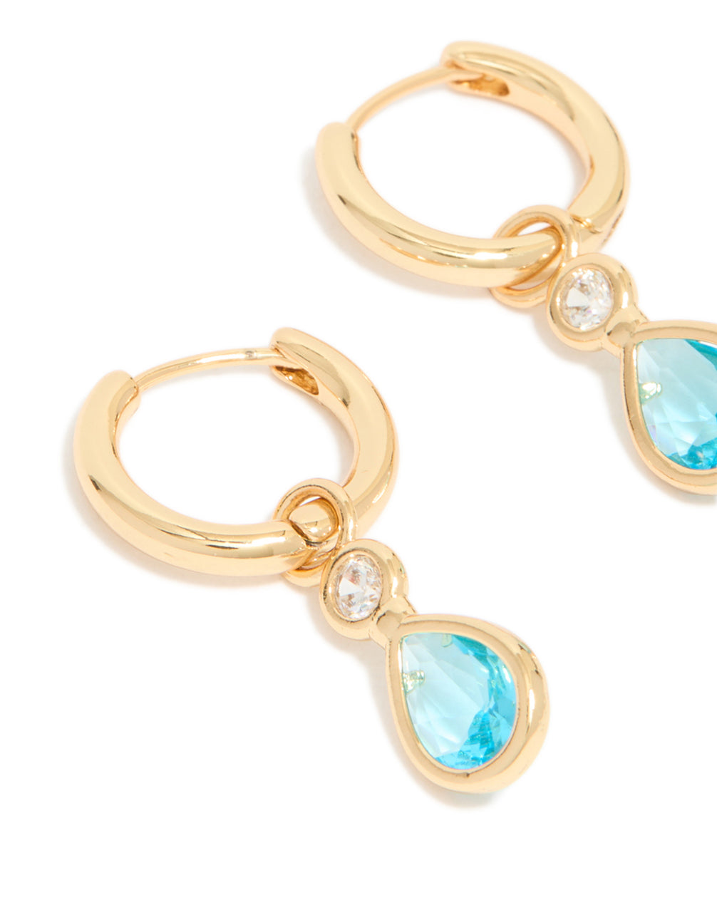 A detailed look at gold-plated blue cubic zirconia teardrop huggie earrings featuring decorative elements and a hoop closure, close up view