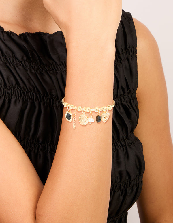 Showcasing a gold heart and black stone charm bracelet with balls, coin and pearl accents on wrist view