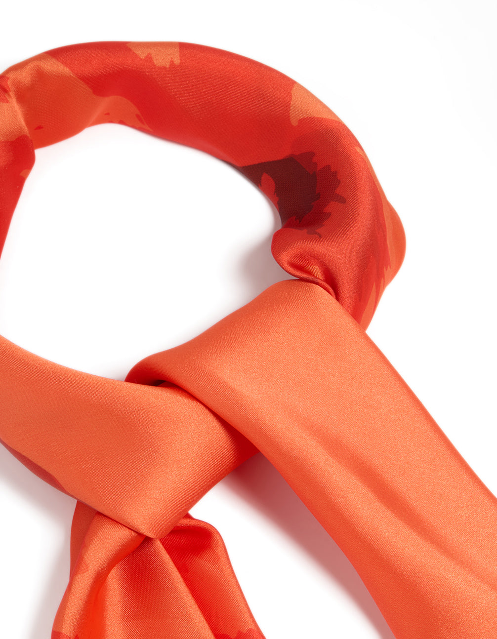 Highlighting an orange fabric scarf with double hibiscus floral print in coral, tomato, and dark orange shades, detail view