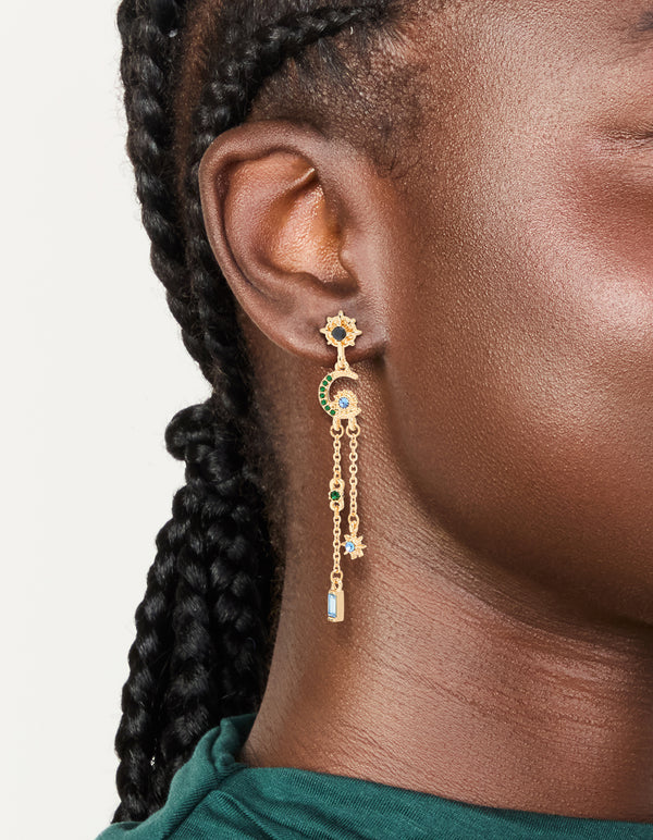 Showcasing gold diamante star and moon chain drop earrings featuring celestial charm design with blue and green accents on ear view