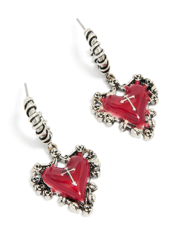 Displaying silver gothic red heart huggie earrings with cross detail and ornate border front view