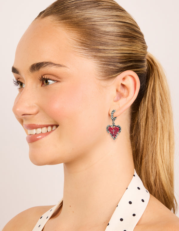Presenting statement gothic huggie hoop earrings in silver featuring crimson heart with cross on model view