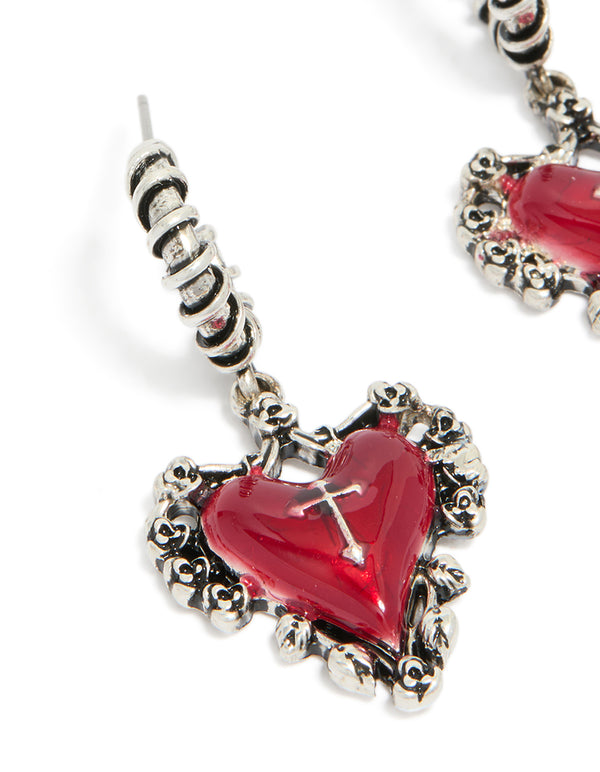 Highlighting detailed craftsmanship of gothic red heart huggie earrings with silver cross and textured frame close up view