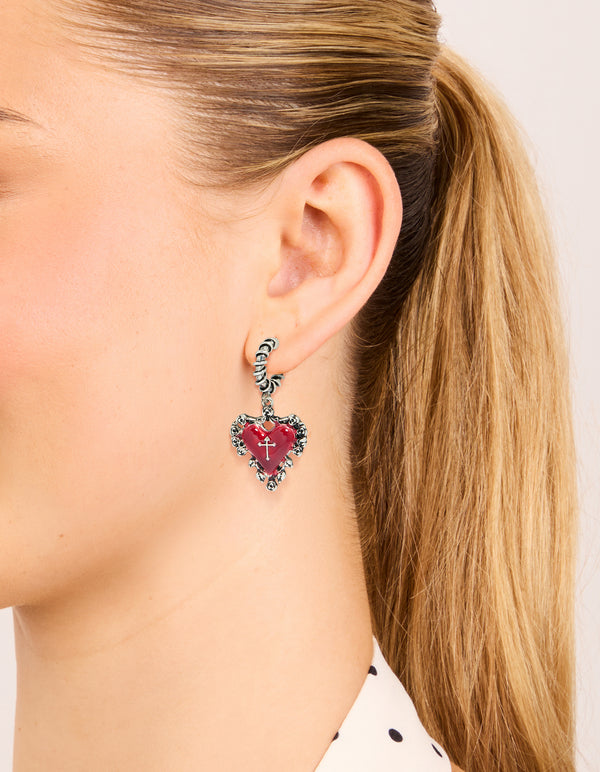 Showcasing gothic style statement huggie hoop earrings with crimson heart featuring silver cross and textured closure on ear view