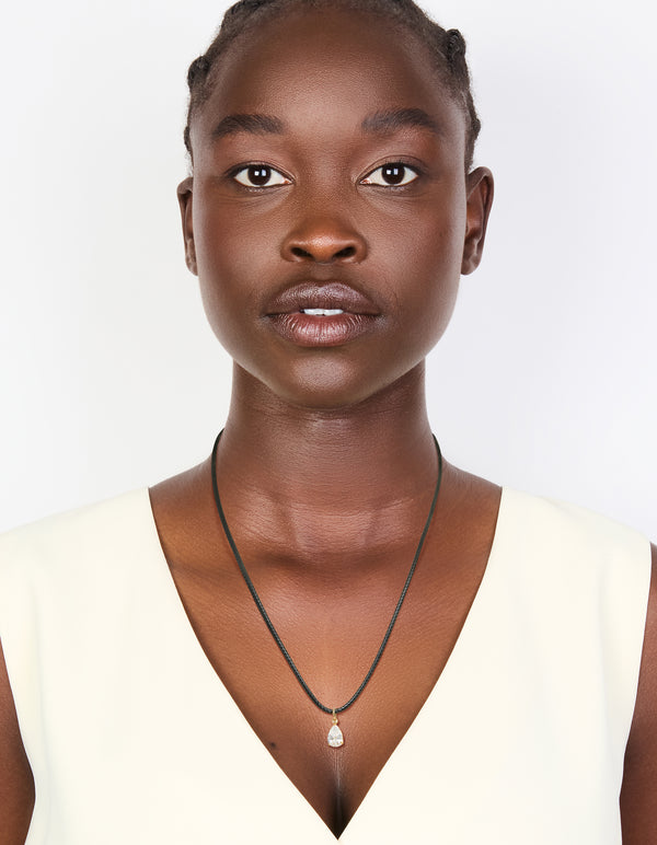 Designed with waterproof charm necklace featuring gold plated stainless steel and black cord and pear cut cubic zirconia pendant in crystal on model view
