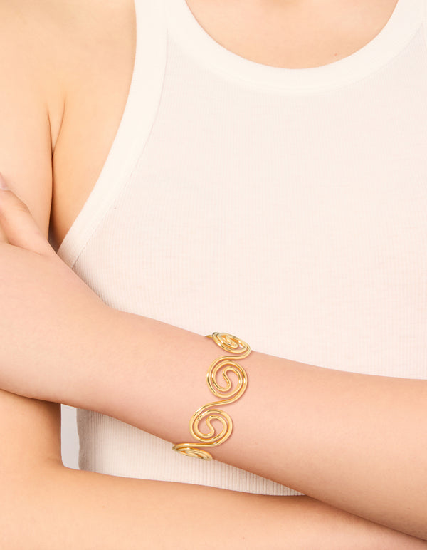 Showcasing a waterproof gold plated stainless steel swirl bendy wrist cuff bangle in statement styling on wrist view