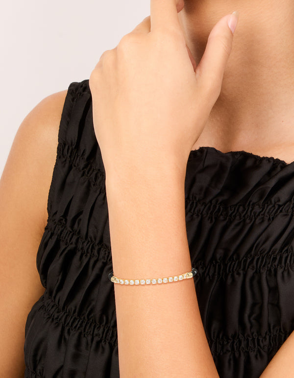 Designed with waterproof gold plated stainless steel, this half tennis and black cord bracelet featuring cubic zirconia details in a statement style on wrist view