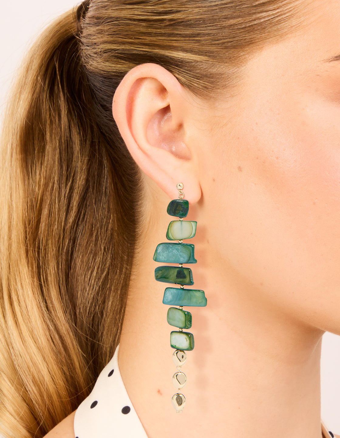 Showcasing dark green acrylic irregular shaped drop earrings featuring beads in teal and pale green with gold accents on ear view