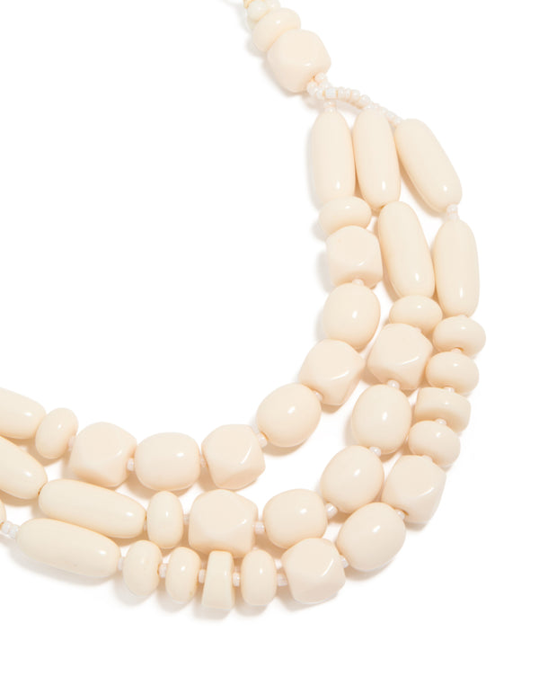Showcasing a beaded acrylic yarn necklace in cream and gold tones close up view