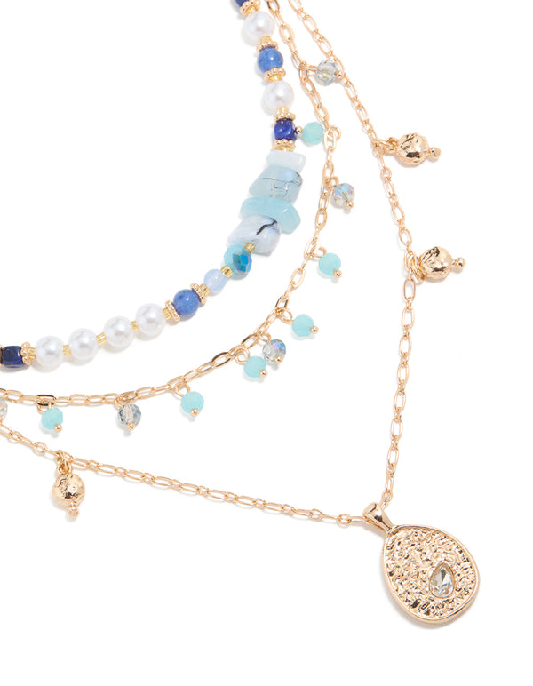 Presenting a stunning layered necklace featuring balls, beads, charm, pendant, and pearls in gold with blue stones close up view