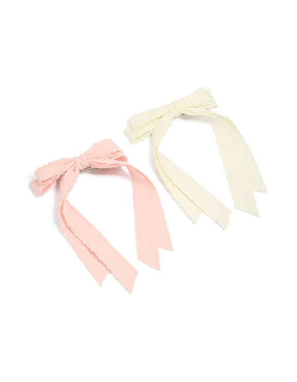 Discover a 2-pack of fabric bow clips with scalloped edges in solid light pink and ivory front view