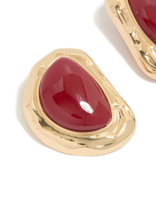 Featuring statement stud earrings with organic textured design and dark red stone in gold finish close up view