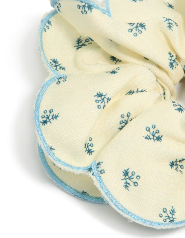 Crafted from fabric with daisy print, this cream blue ruffled scrunchie in ivory, sky blue and teal detail view