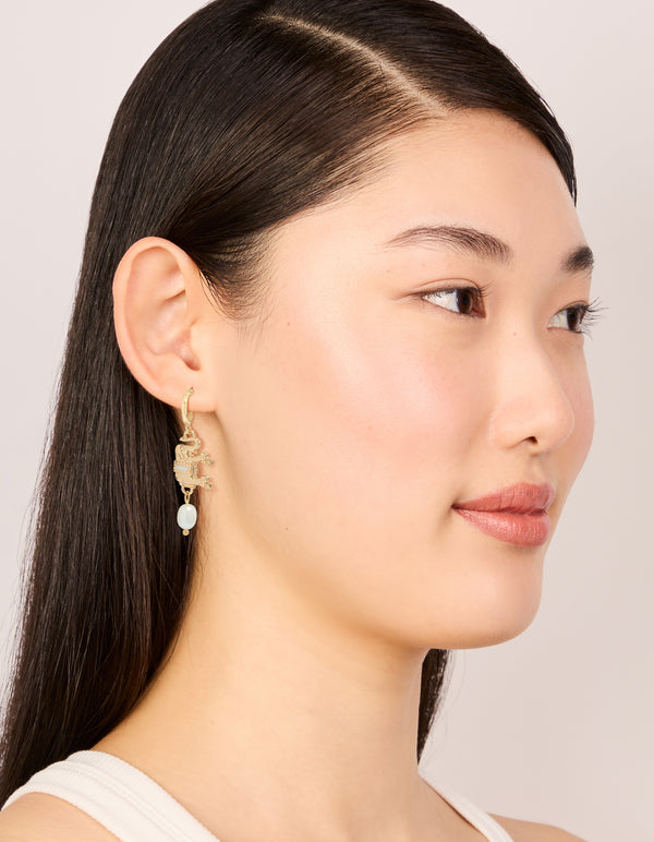 Crafted gold hoop earrings featuring a freshwater pearl and an animal elephant charm with ivory accents on model view