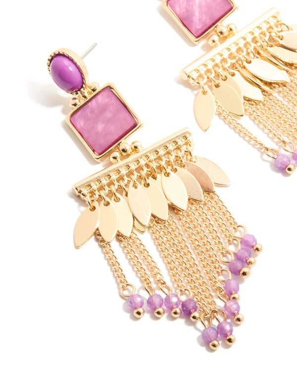 Featuring gold statement drop earrings with purple beaded chain tassels, and leaf charm accents close up view
