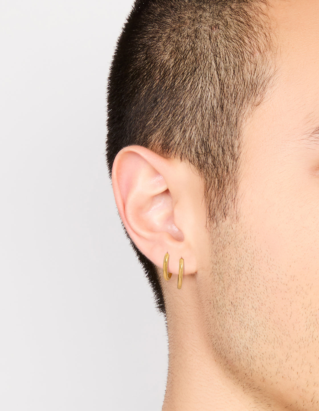 Featuring mens waterproof gold plated stainless steel mixed size huggie earrings 2-pack on ear view