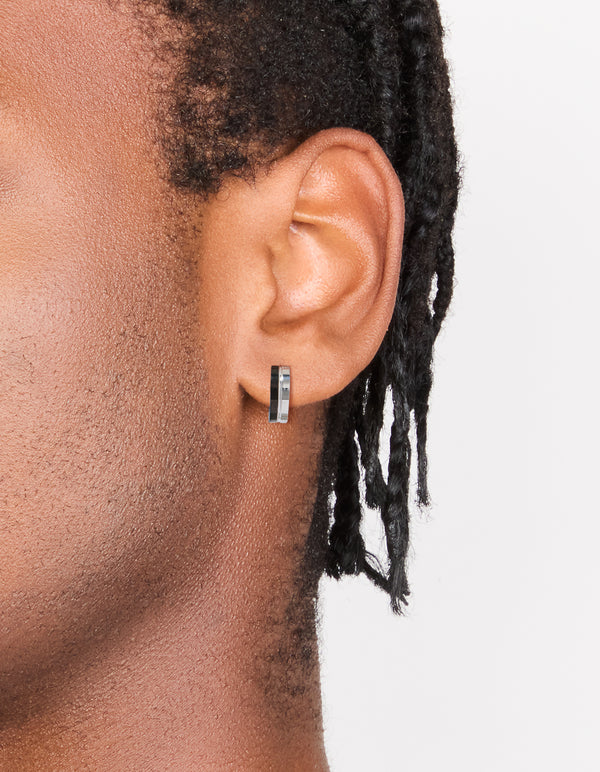 Featuring men's waterproof stainless steel huggie earrings with black enamel inlay in statement style on ear view