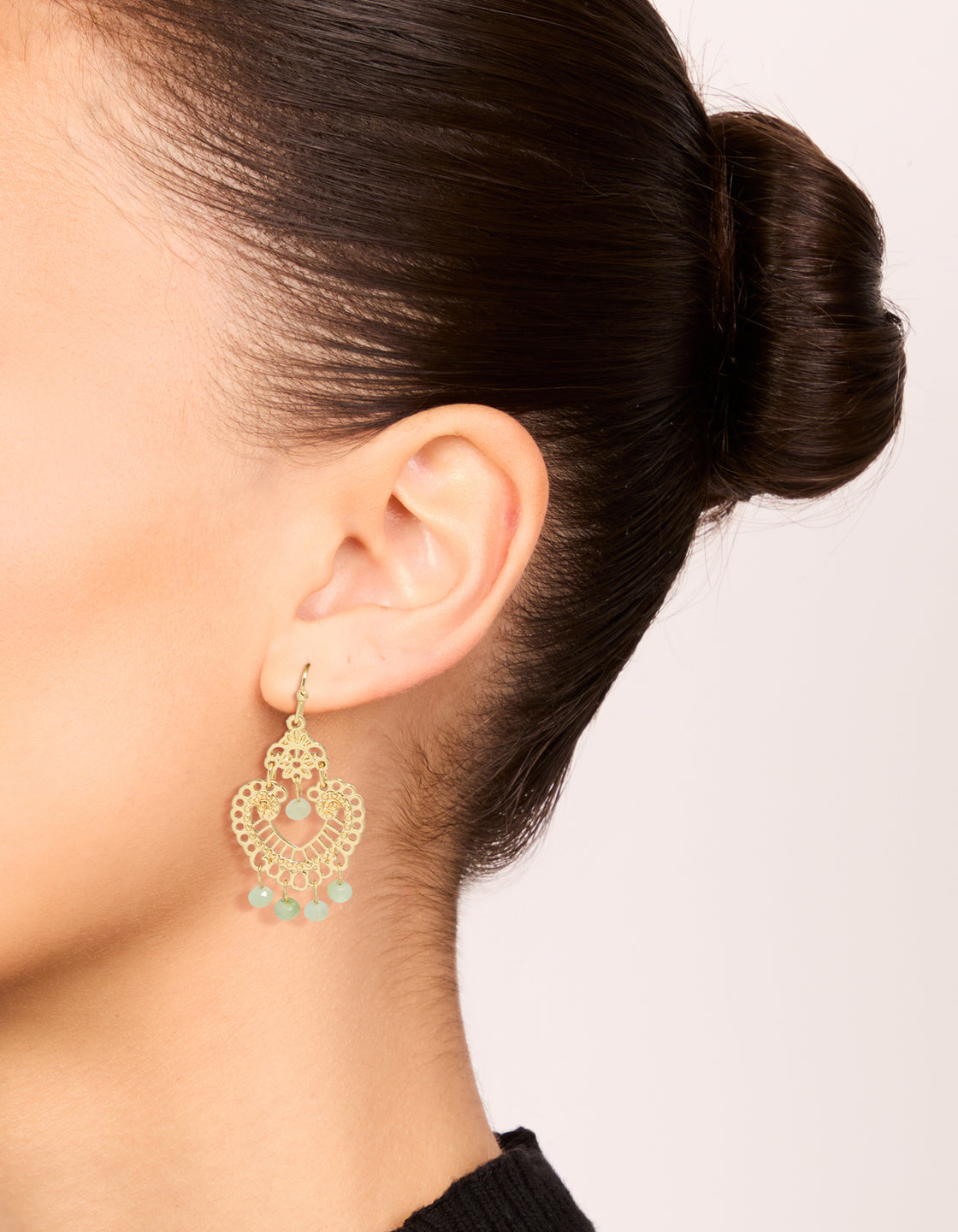 Crafted from gold plated material, these decorative drop earrings with charm beads and pale green semi precious stones on ear view