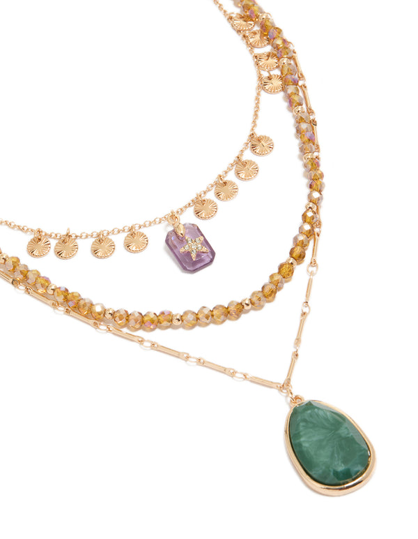 This gold celestial star, beaded chain layered necklace features charms, disc accents, pendant drops, and oval stone details in a close up view