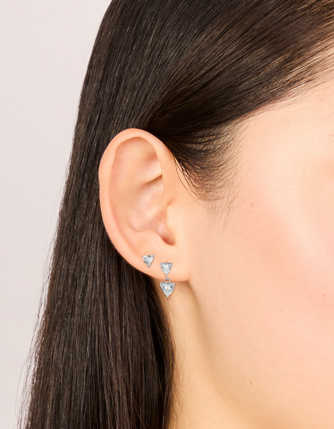 Featuring waterproof stainless steel cubic zirconia heart stud and drop earrings in a 2-pack with silver and clear tones on ear view