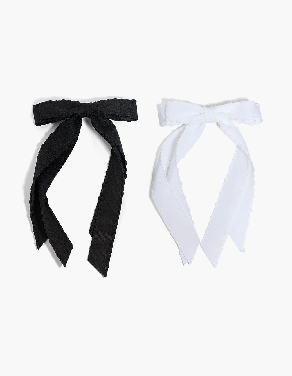 Showcasing a 2-pack of fabric bow clips with scalloped edges in solid white and black front view