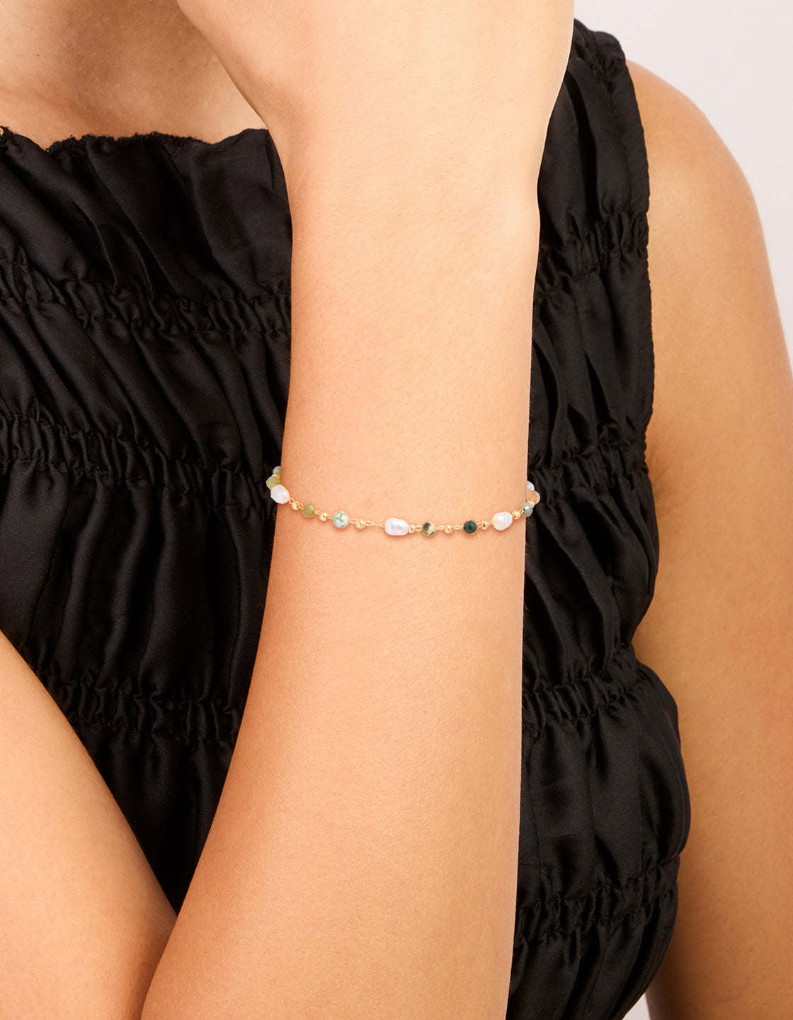 Showcasing a gold plated bracelet with green beads and pearls on wrist view