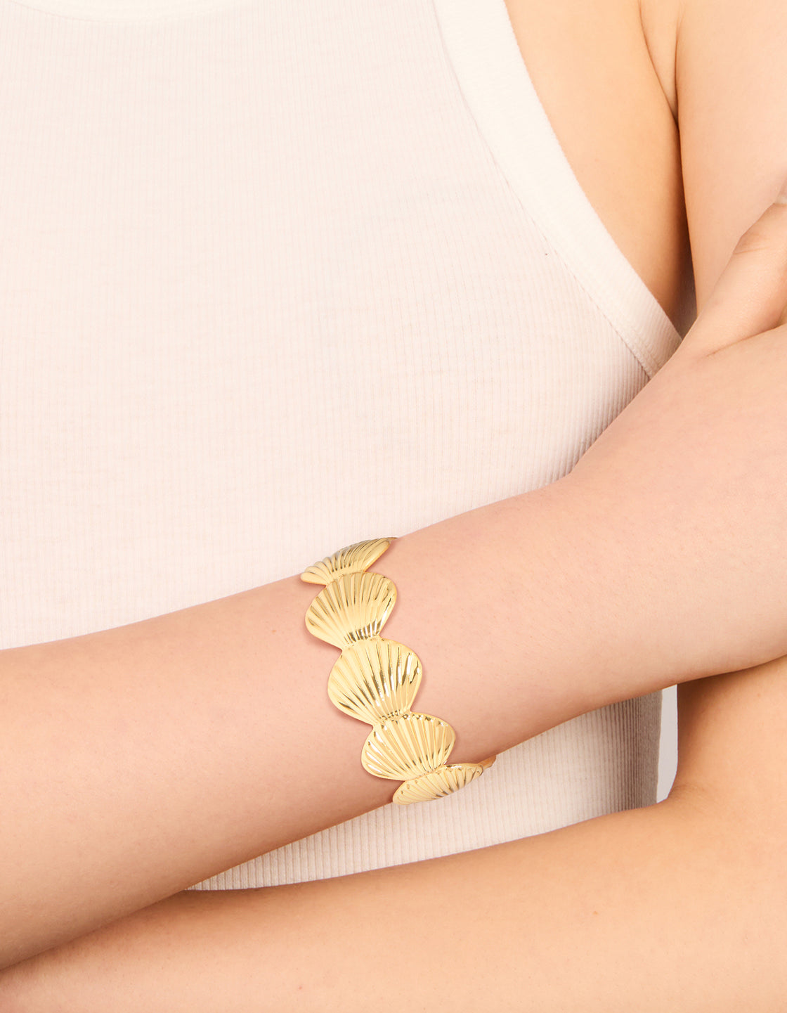 Showcasing a gold plated shell statement wrist cuff with ocean-inspired chunky bracelet on wrist view
