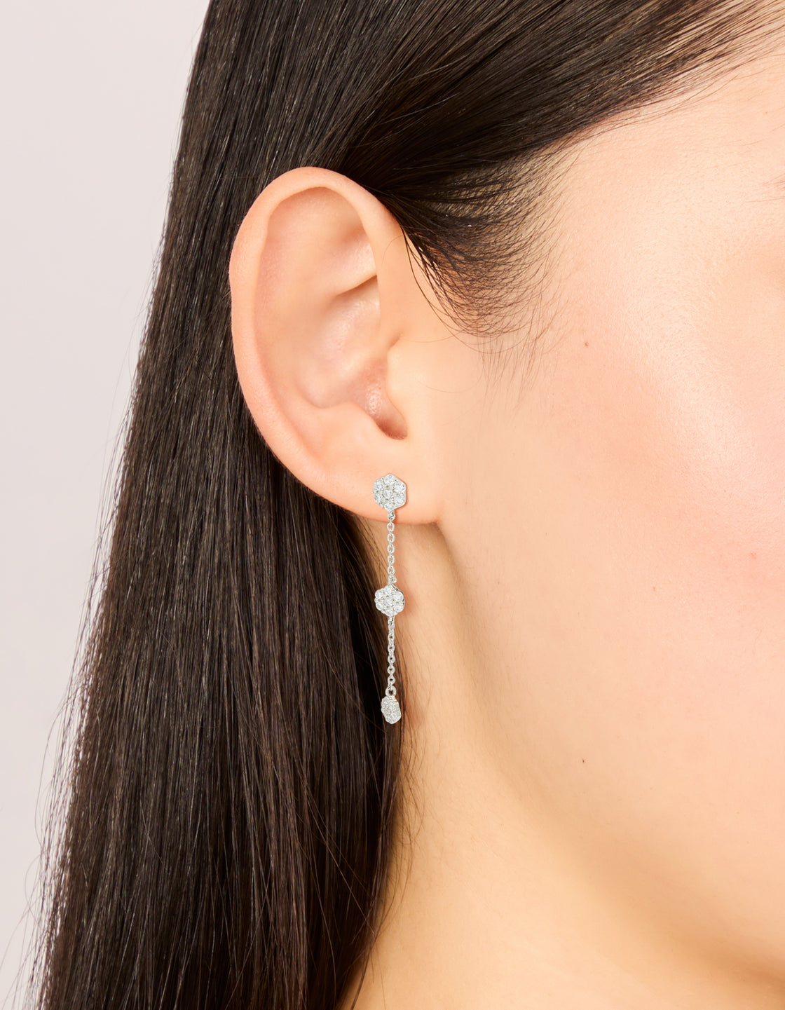 Showcasing silver cubic zirconia mini floral drop earrings with delicate chain design on ear view