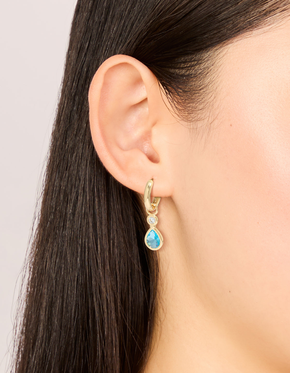 These gold plated teardrop huggie earrings feature blue cubic zirconia with a hoop closure on ear view
