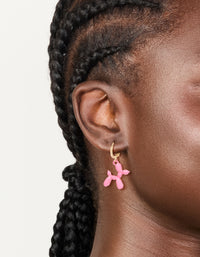 Showcasing huggie earrings in gold with pink balloon dog animal worn on ear view - link has visual effect only