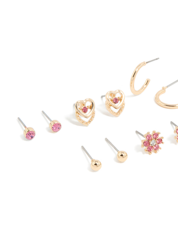 Featuring stud earrings 7-pack with balls, floral, butterfly, and heart motifs in gold with hot pink diamante stones close up view