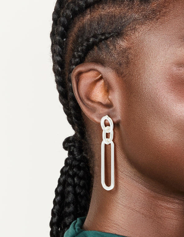 Showcasing large statement drop earrings with oval link design in silver plated material on ear view
