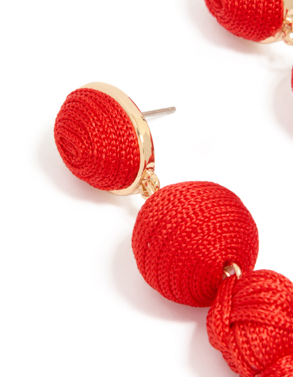 Elegant statement tassel drop earrings in red fabric with gold detailing close up view