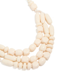 Showcasing a beaded acrylic yarn necklace in cream and gold tones close up view - link has visual effect only